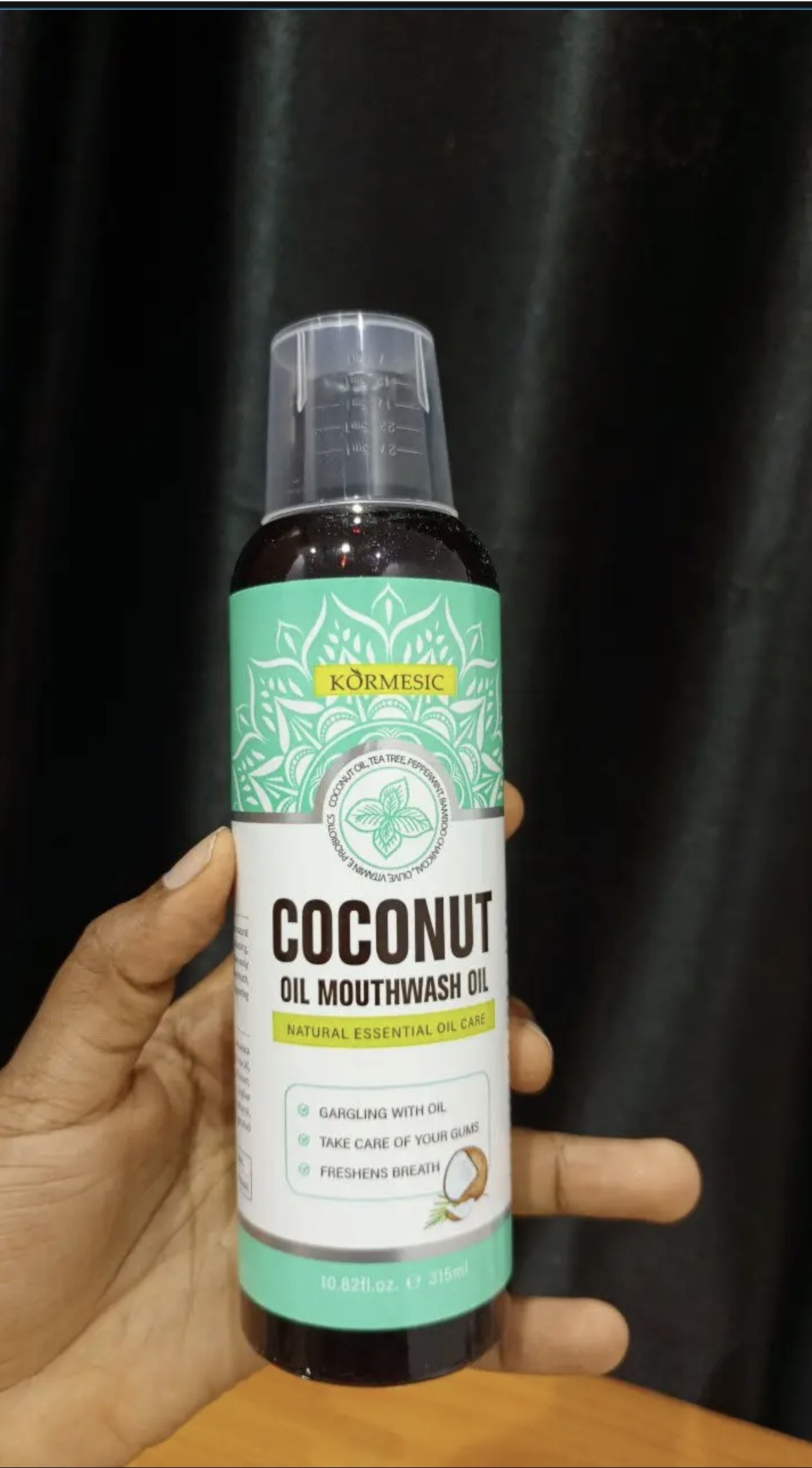 Kormesic Coconut Oil Mouthwash bottle held up showing the label, coconut oil, tea tree, peppermint, bamboo charcoal formula